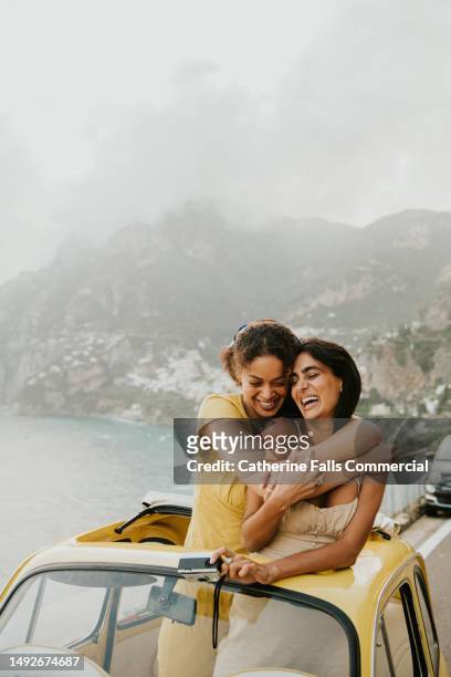two woman enjoy experiential travel in a rented vintage car in italy. they hug. - travel stock-fotos und bilder