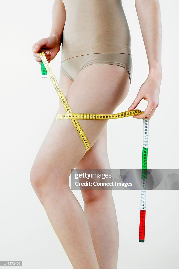 Young woman measuring thigh with tape measure