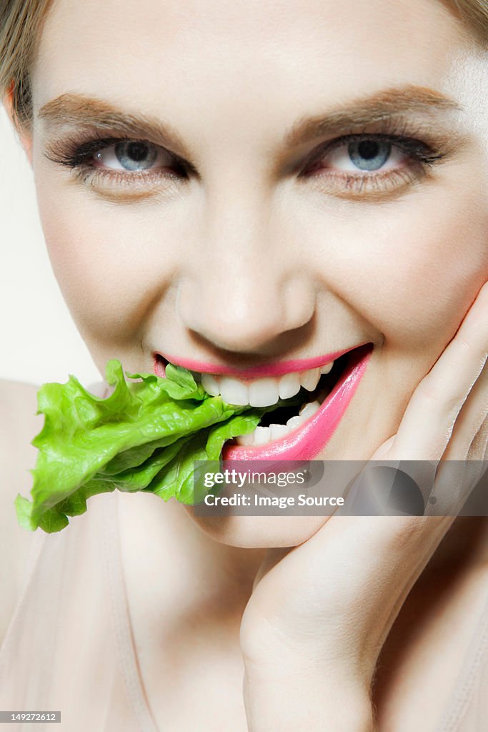 Young woman biting lettuce