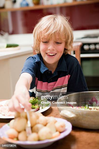 young boy at the family dinner table helping himself to potatoes - gekookte aardappel stockfoto's en -beelden