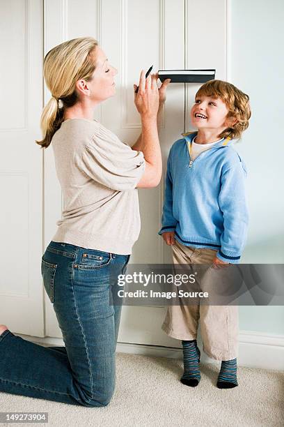 mother measuring her son against a door with a book - growth chart stock pictures, royalty-free photos & images