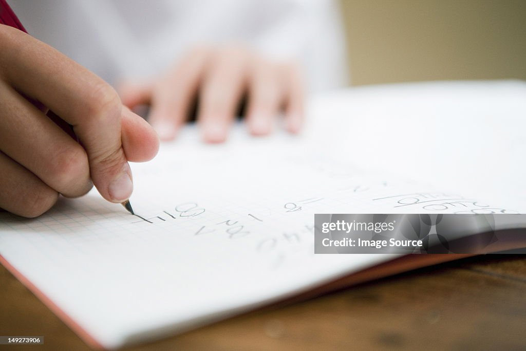 Close up of the hands of a young boy writing in a textbook