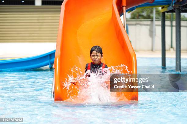 little boy sliding in a swimming pool joyfully - water slide stock pictures, royalty-free photos & images