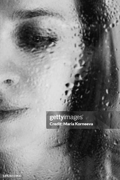 pensive woman looking through window on rainy day. - wet see through fotografías e imágenes de stock