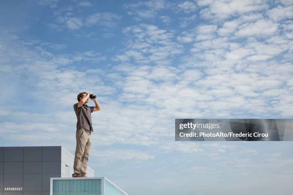 Oversized man standing on rooftop, looking through binoculars