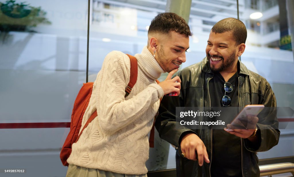 Friends laughing at something on a phone while waiting at a bus stop