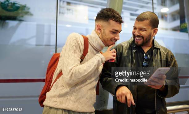 friends laughing at something on a phone while waiting at a bus stop - lgbtqi stock pictures, royalty-free photos & images