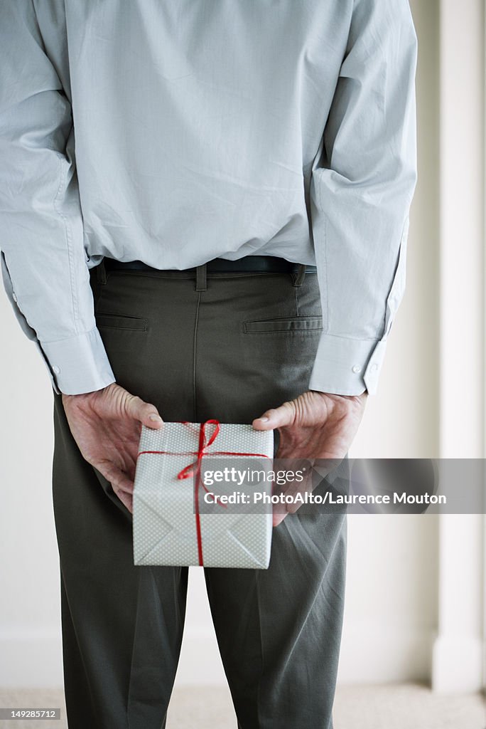 Man holding wrapped gift behind his back, cropped