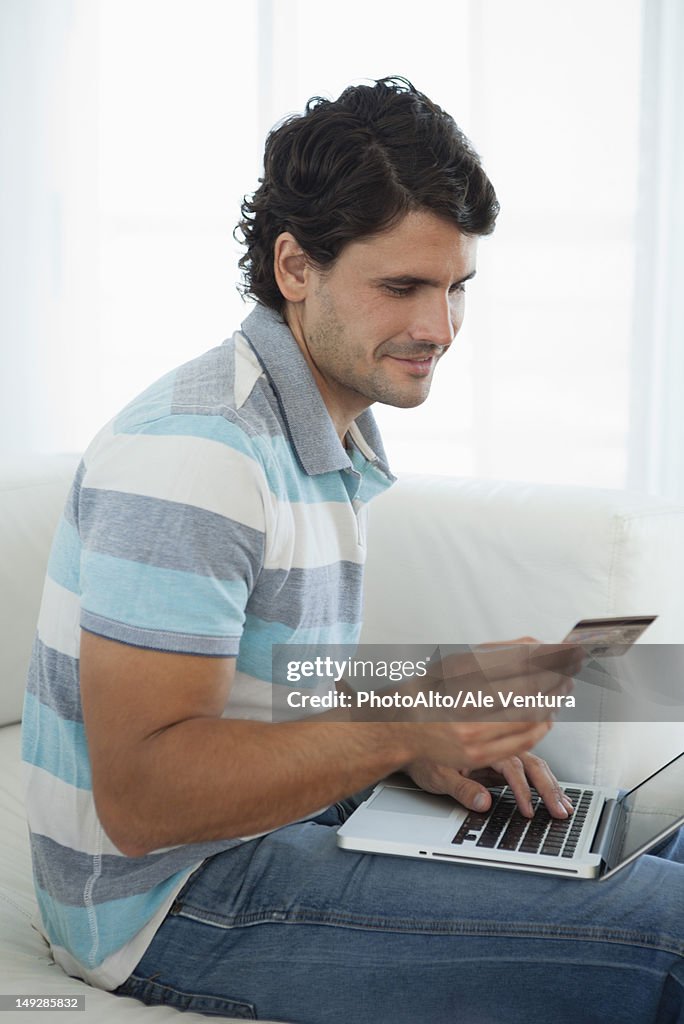 Mid-adult man holding credit card while using laptop computer