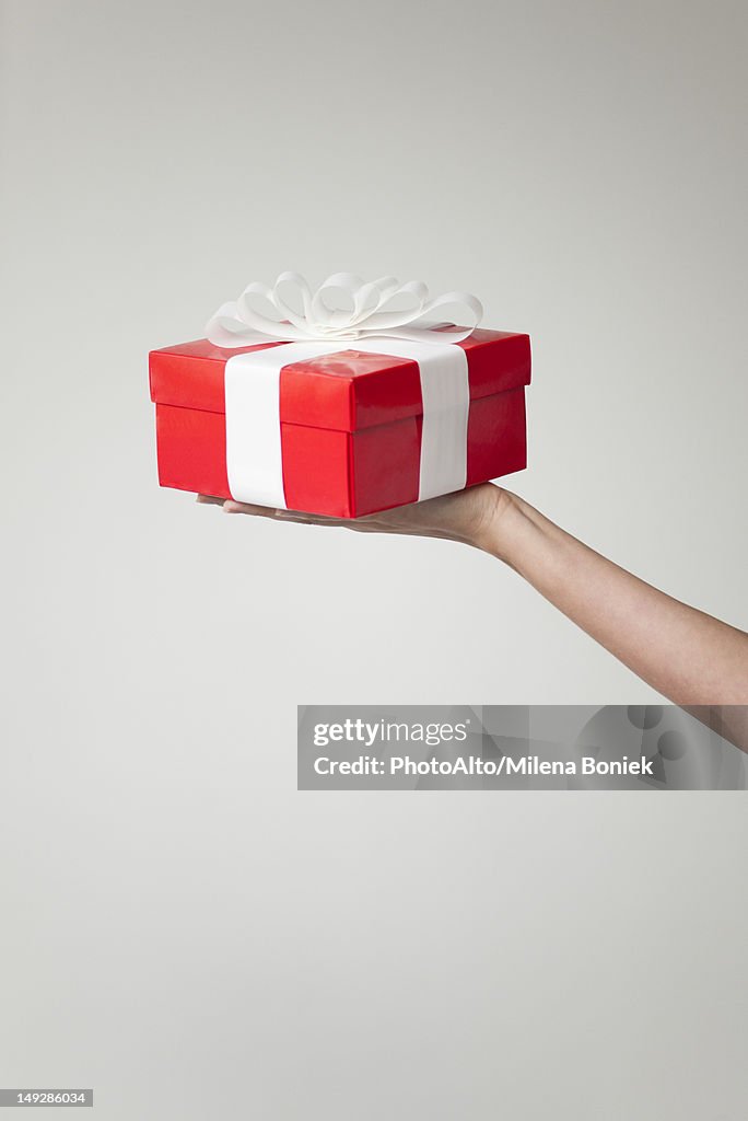 Woman's arm holding out gift box, cropped