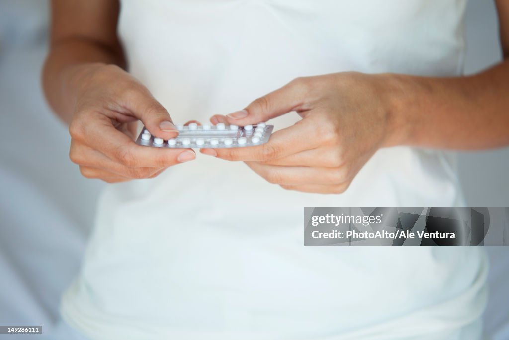 Woman holding birth control pills, mid section
