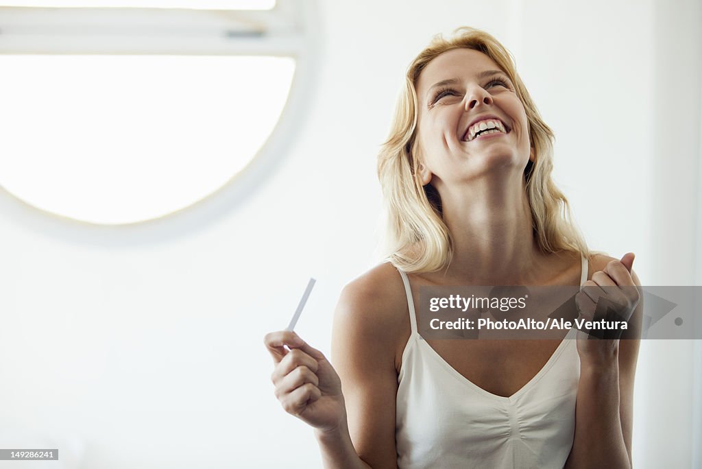 Young woman holding pregnancy test, laughing