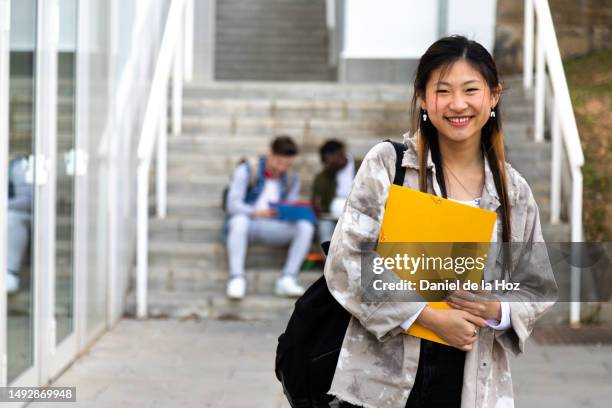happy smiling female asian teen college student on campus holding books looking at camera. copy space. - laatstejaars high school stockfoto's en -beelden