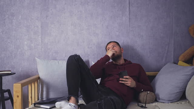 Young Bearded Man Reflecting on Life with Phone in Hand while Laying Down