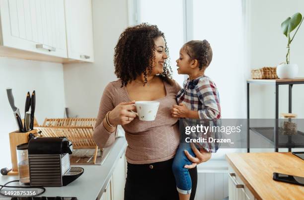 multiracial afro-caribbean mother holding her girl and making coffee in the kitchen. - een dag uit het leven serie stockfoto's en -beelden