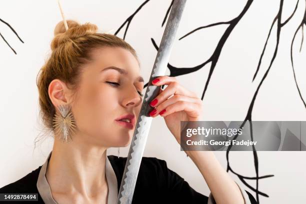 attractive girl in kimono and hair sticks against white background with tree branches holds katana sword - ninja sword stock pictures, royalty-free photos & images