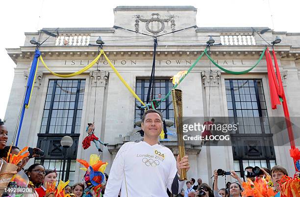 In this handout image provided by LOCOG, Torchbearer 024 David Walliams holds the Olympic Flame in front of Islington Town Hall, during Day 69 of the...