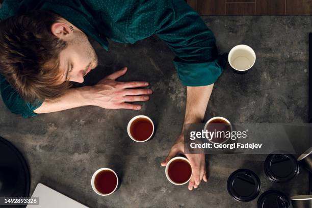 sleepy man addicted to coffee cant stop drinking, indoor in the kitchen, many cups scattered around a table. caffeine addiction concept. top view - addiction stock pictures, royalty-free photos & images