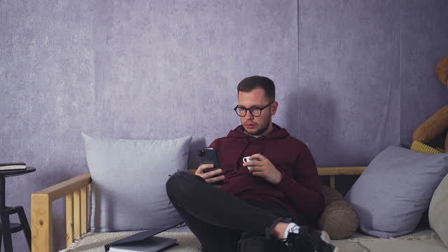Young Male Unwinding with Smartphone and Coffee in Comfortable Living Room