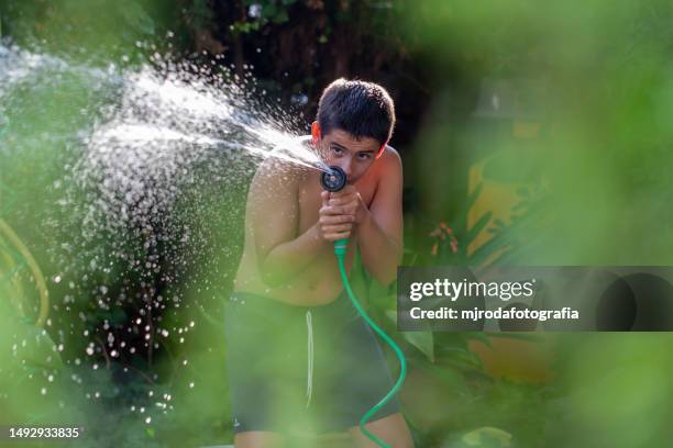 boy playing with water from a hose in the garden - hose stock pictures, royalty-free photos & images