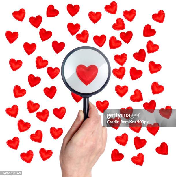 female fingers hold a magnifying glass over a red heart ornament from many hearts - escape rom stock pictures, royalty-free photos & images