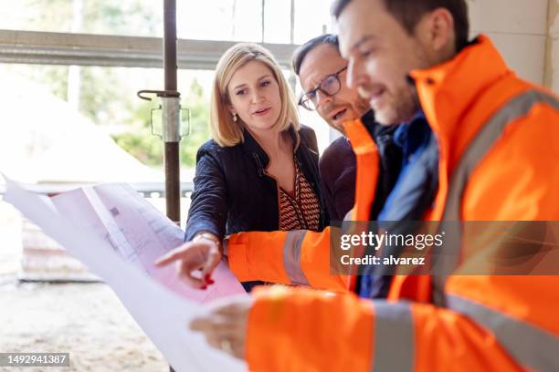 male architect showing new apartment construction blueprints to a couple - construction site stock pictures, royalty-free photos & images