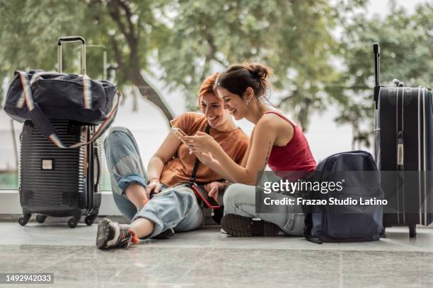 young friends woman using phone sitting on ground while waiting at airport - argentina travel stock pictures, royalty-free photos & images