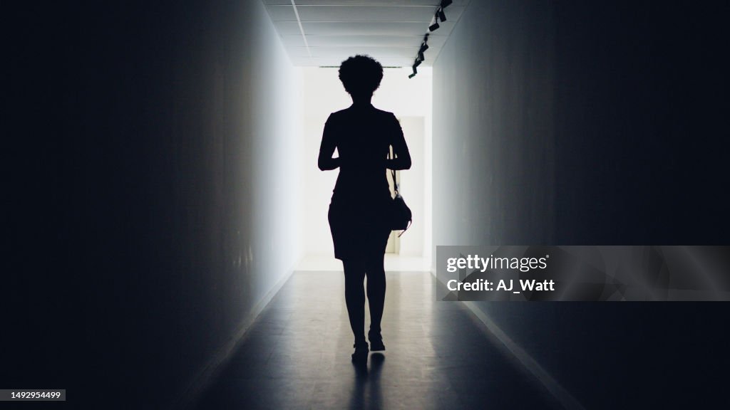 Silhouetted businesswoman walking down a dark corridor to doorway