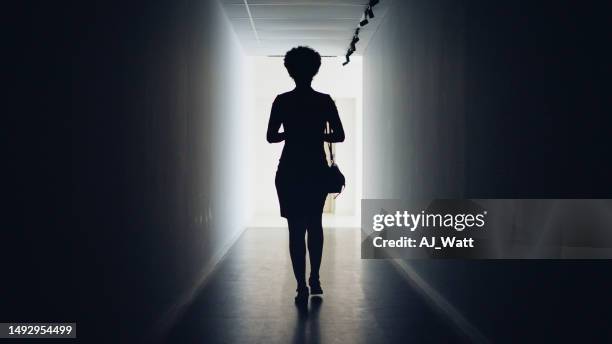 silhouetted businesswoman walking down a dark corridor to doorway - woman walking out door silhouette stock pictures, royalty-free photos & images