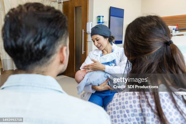 over-the-shoulder view midwife sharing baby care tips with unrecognizable couple - midwife stock pictures, royalty-free photos & images