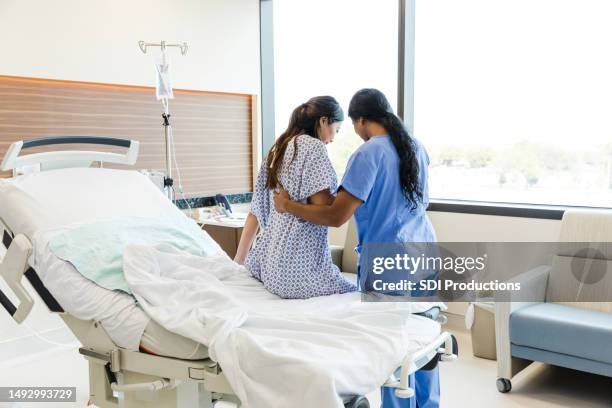unrecognizable female nurse helps woman get out of hospital bed - nurse stockfoto's en -beelden