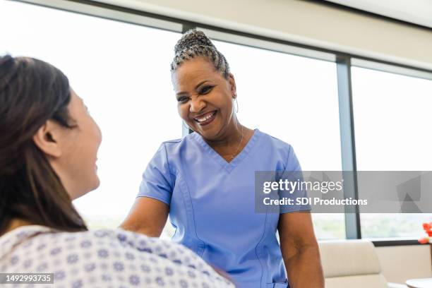 female patient and female nurse smile at each other - er visit stock pictures, royalty-free photos & images