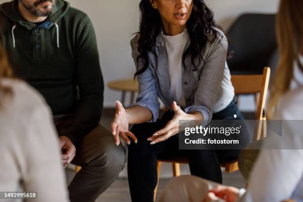 anxious young woman sharing her struggles with her peers during a group therapy session - onderhandelen stockfoto's en -beelden