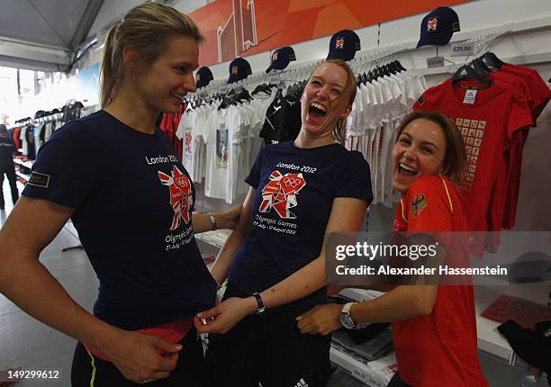 Fencers Britta Heidemann, Ricarda Multerer and Monika Sozanska of Germany laugh while trying shirts in the merchandising store at the Olympic Village...