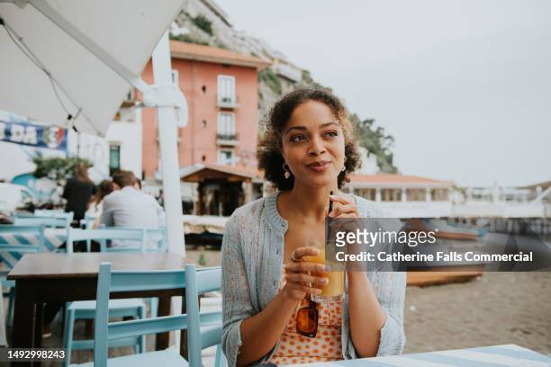 a woman sips on a juice at an outdoor cafe - no alcohol stock-fotos und bilder