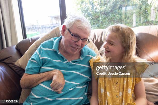 smiling senior man with dementia sitting on sofa with smiling young girl - miembro humano fotografías e imágenes de stock