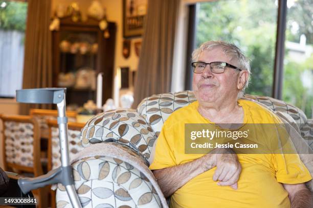 senior man with dementia sitting in armchair, with crutch, looking to side - sistema inmunocomprometido fotografías e imágenes de stock