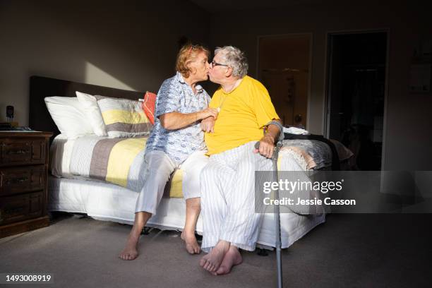 senior man with dementia sitting on bed kissing senior woman, in sunshine - medical alert tag stock pictures, royalty-free photos & images