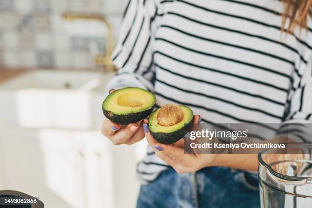 unrecognizable woman preparing healthy detox drink in a blender: green smoothie with banana, spinach and avocado while standing at kitchen desk - avocado smoothie stock pictures, royalty-free photos & images