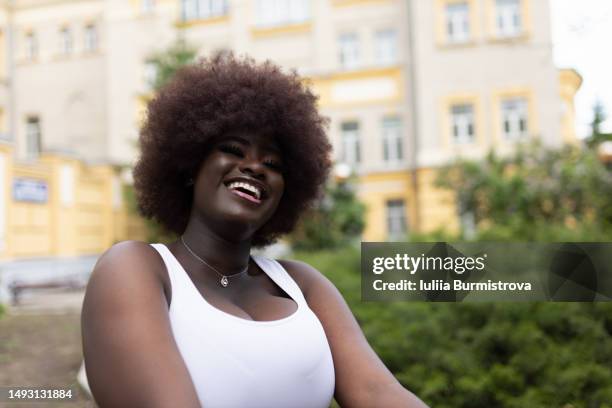 feminine black lady with brown hair in white top laughing with yellow building in background - sleeveless stock pictures, royalty-free photos & images