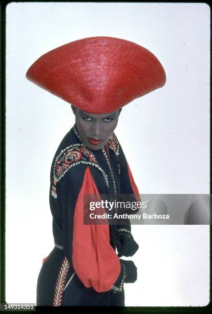 Portrait of Jamaican-born model, singer, and actress Grace Jones as she wears a bright red hat and multi-colored top, New York, New York, late...