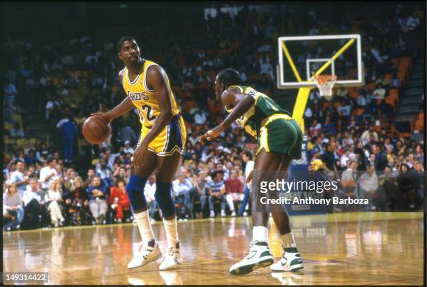 American basketball player Magic Johnson , of the Los Angeles Lakers, dribbles the ball as he looks up court, his path blocked by Nate McMillian, of...