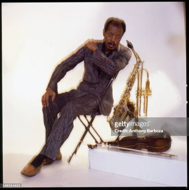 Portrait of American jazz musician and composer Ornette Coleman as he sits in a chair against a white background, surround by three of his...