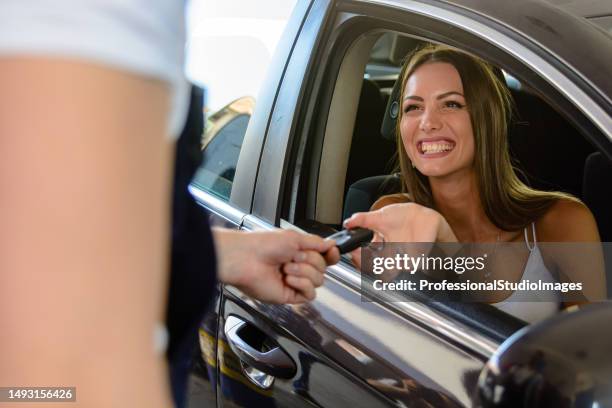 glückliche junge frau sitzt in einem auto und übernimmt nach dem gottesdienst einen schlüssel aus einem auto. - happy client by broken car stock-fotos und bilder