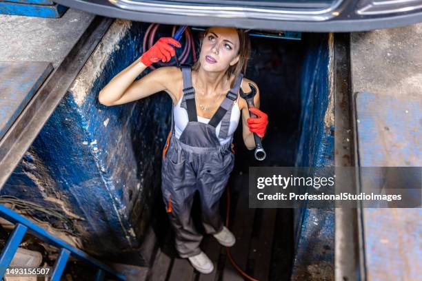 a mechanic woman is working underside a car in canal using a mechanic equipment. - adjustable wrench stock pictures, royalty-free photos & images