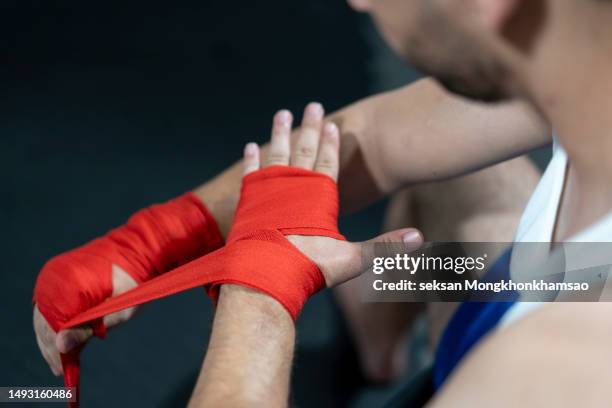 young muscular unrecognisable male putting on boxing bandages before the training session - artes marciales mixtas fotografías e imágenes de stock