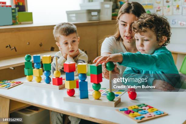 female teacher helping little boy sort the cubes by color in a kindergarten - niño de edad preescolar fotografías e imágenes de stock
