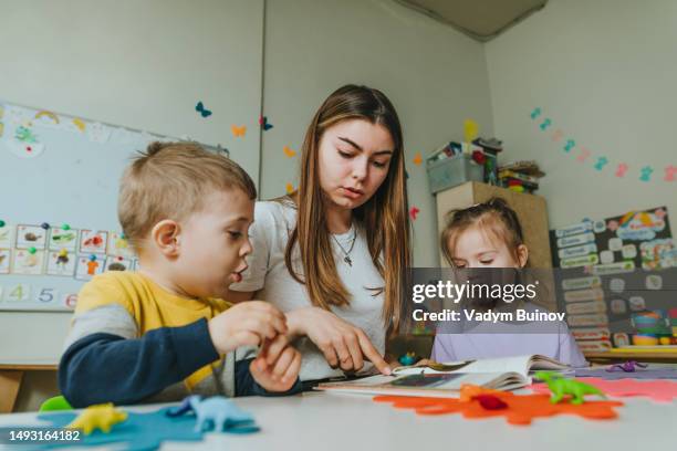 teacher reading book to children sitting at the table in kindergarten - child care worker stock pictures, royalty-free photos & images