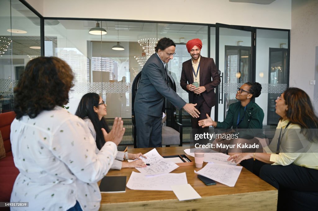 Senior manager congratulating the African mid-adult colleague on the successful completion of the project in a meeting room