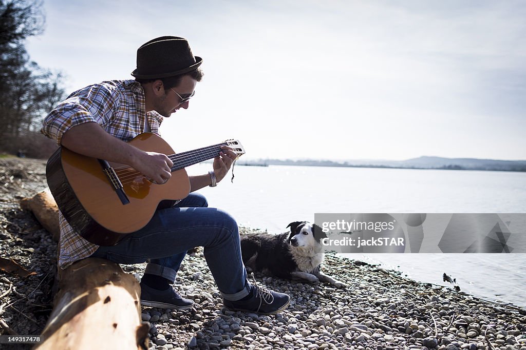 Man playing guitar with dog by creek